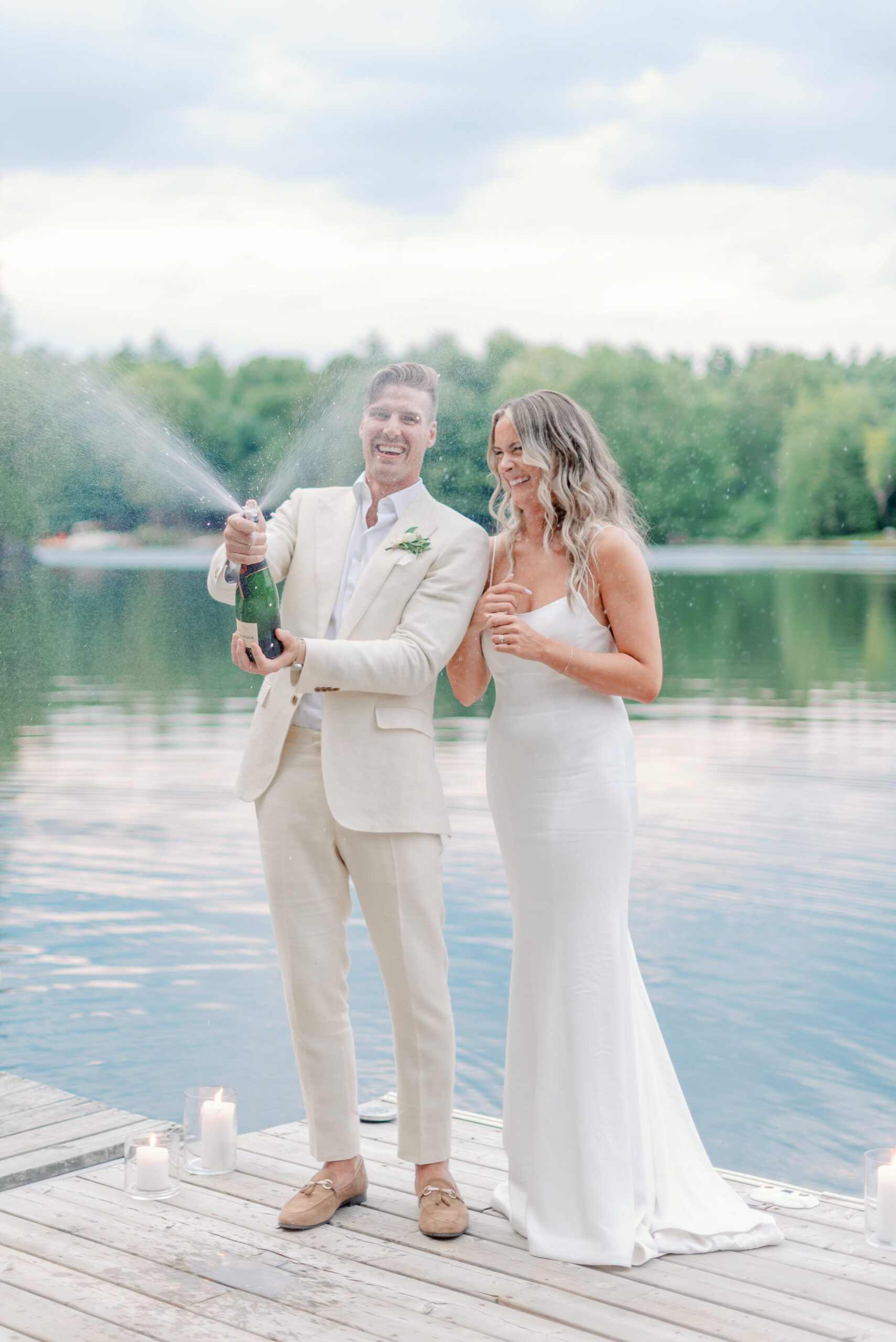 Wedding couple popping champagne bottle on edge of dock on Muskoka Lake.