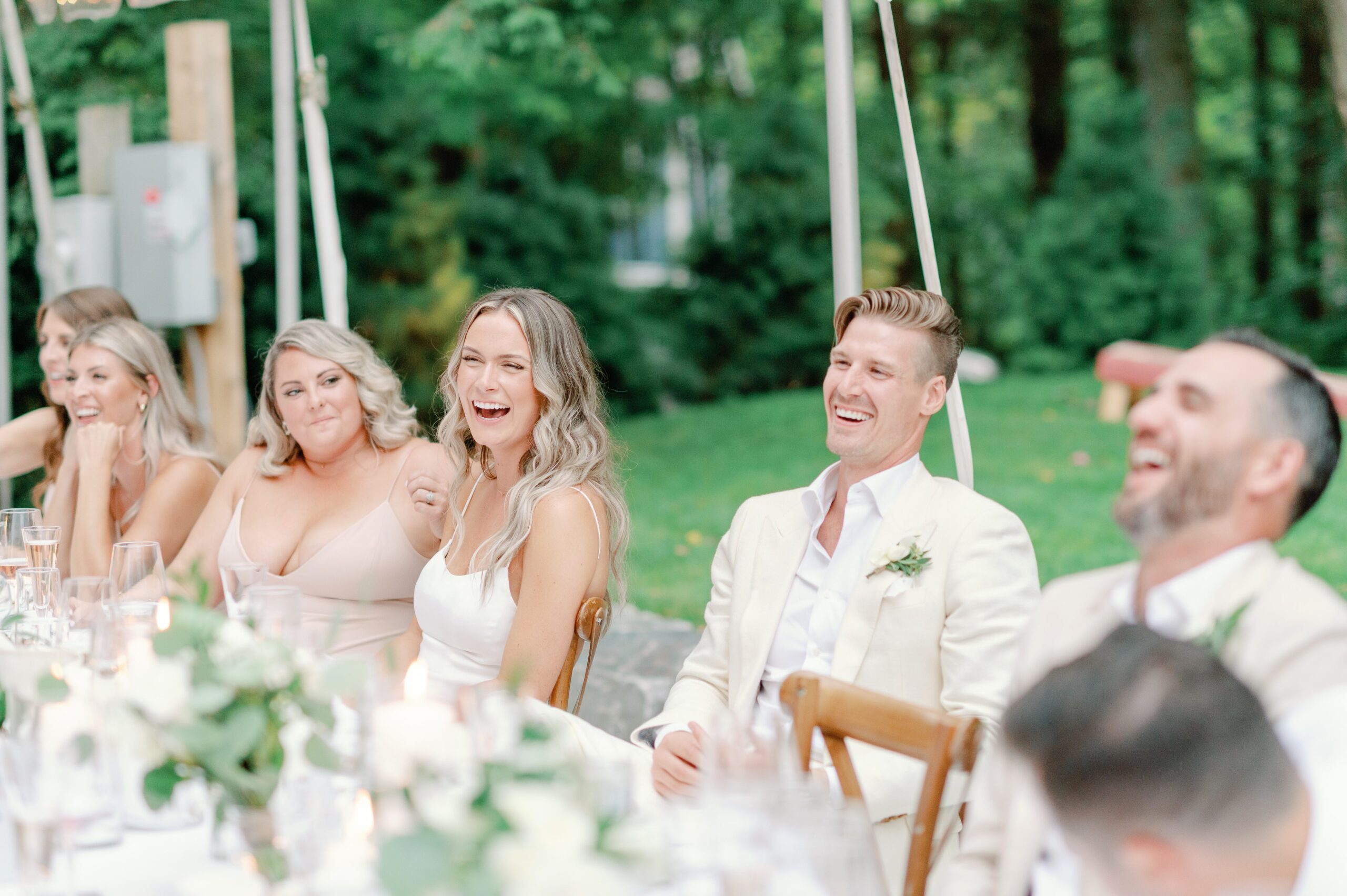 Candid moment of head table laughing at outdoor wedding reception.