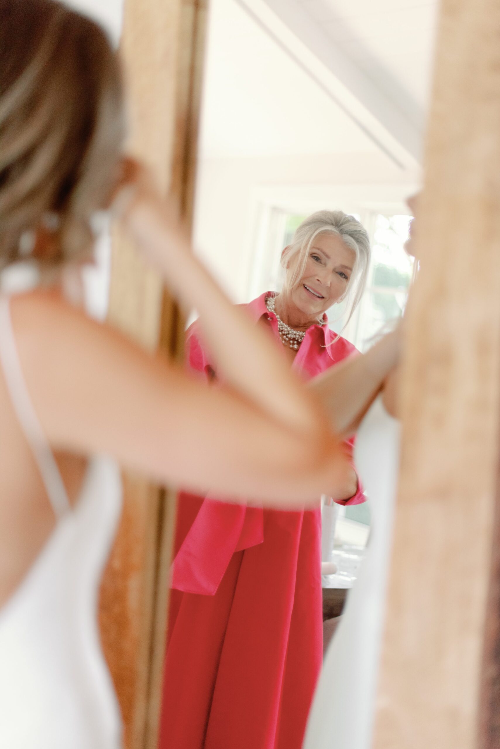 Mother helping bride get ready in mirror.