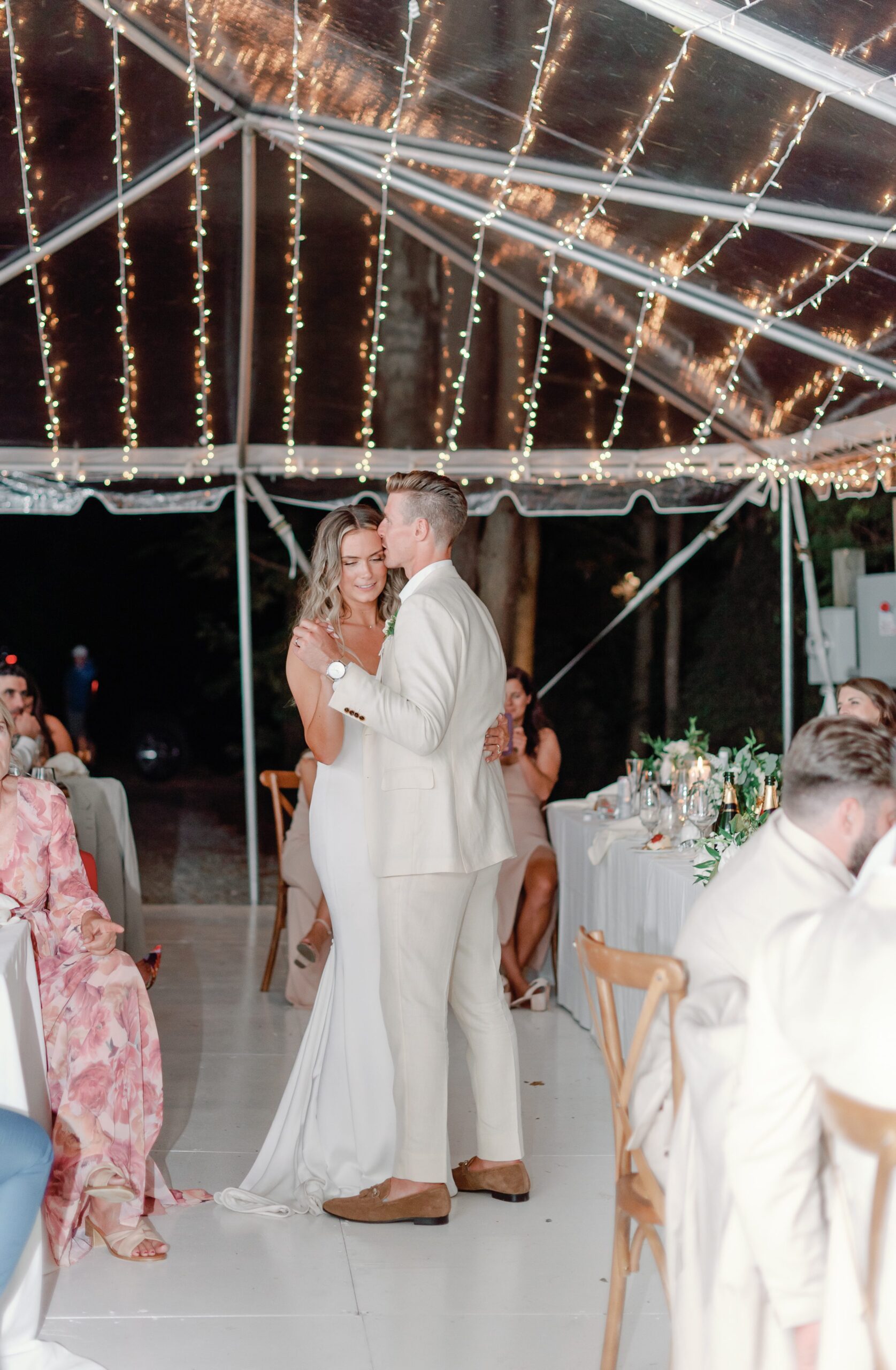First dance under clear wedding tent with string lights.