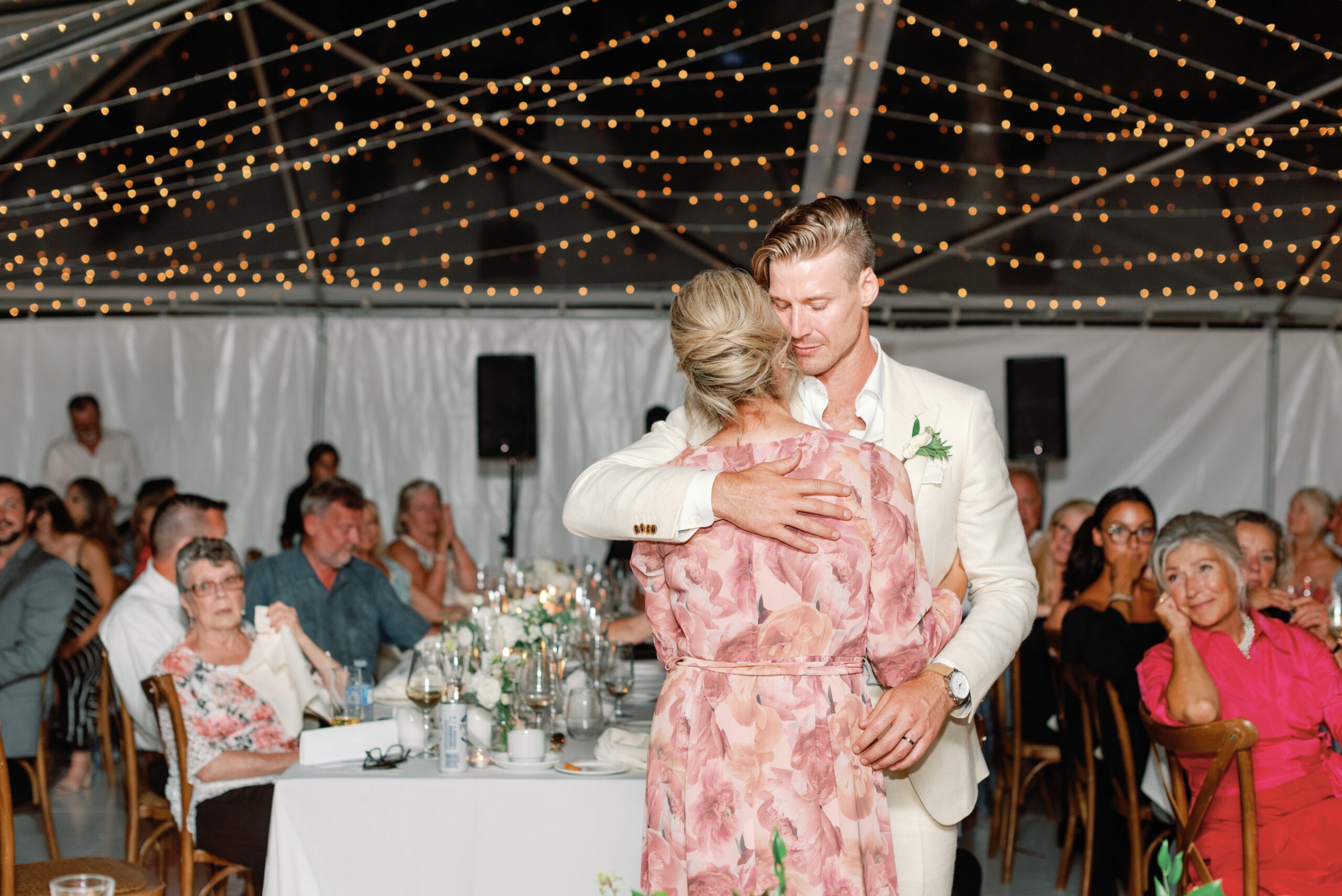 Sweet moment of groom dancing with mother at wedding under string lights.